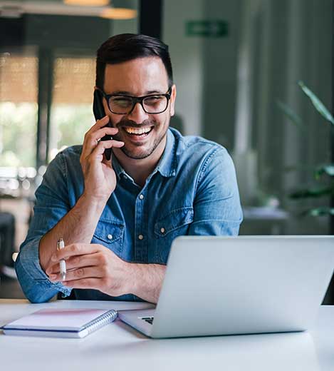young smiling cheerful entrepreneur in casual office making phone call while working with laptop